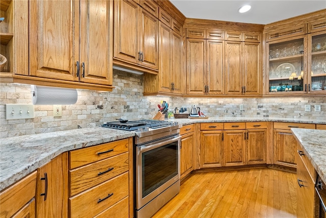 kitchen featuring light stone countertops, tasteful backsplash, high end stainless steel range, and light hardwood / wood-style floors