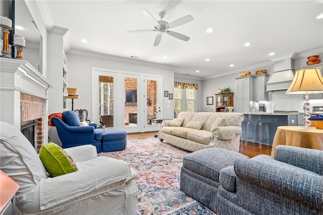 living room featuring ceiling fan, ornamental molding, hardwood / wood-style floors, and a brick fireplace