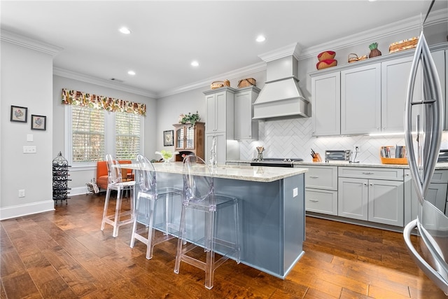 kitchen featuring a kitchen breakfast bar, custom exhaust hood, a kitchen island with sink, light stone countertops, and dark wood-type flooring