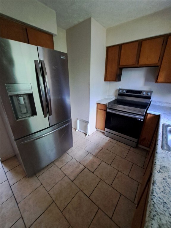 2106 Auburn St, Tuskegee, AL 36083 - kitchen featuring light tile patterned floors, brown cabinets, light countertops, and stainless steel appliances
