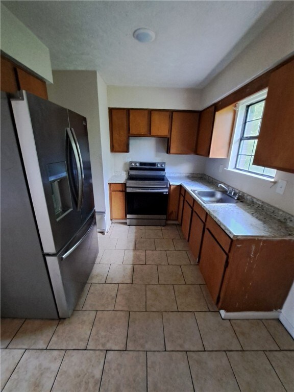 2106 Auburn St, Tuskegee, AL 36083 - kitchen featuring brown cabinets, a sink, stainless steel electric range, refrigerator with ice dispenser, and light countertops