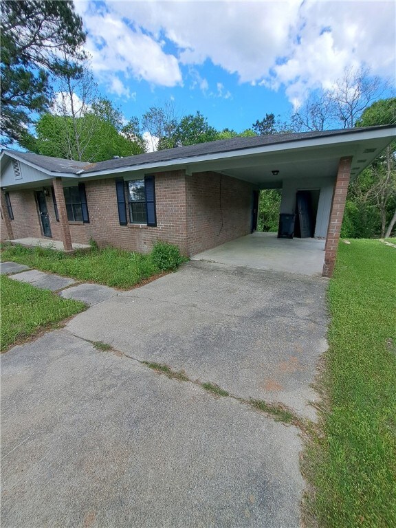 2106 Auburn St, Tuskegee, AL 36083 - exterior space featuring a yard, brick siding, driveway, and an attached carport