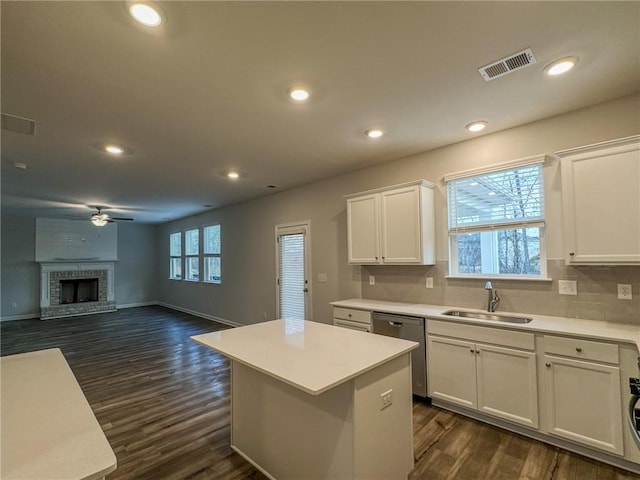 kitchen with a fireplace, a sink, visible vents, white cabinets, and stainless steel dishwasher