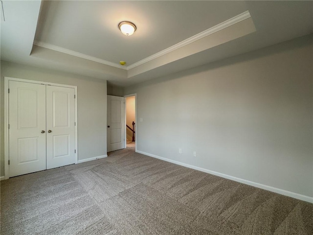 unfurnished bedroom with carpet floors, a raised ceiling, crown molding, and baseboards