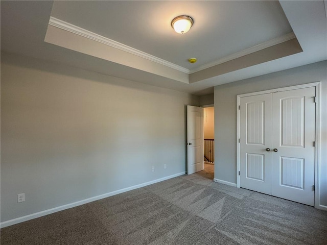 unfurnished bedroom with ornamental molding, a tray ceiling, carpet, and baseboards