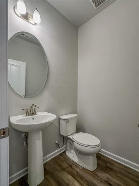 half bath featuring baseboards, visible vents, toilet, and wood finished floors