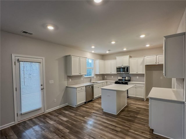 kitchen featuring dark wood-style flooring, a kitchen island, a sink, visible vents, and appliances with stainless steel finishes