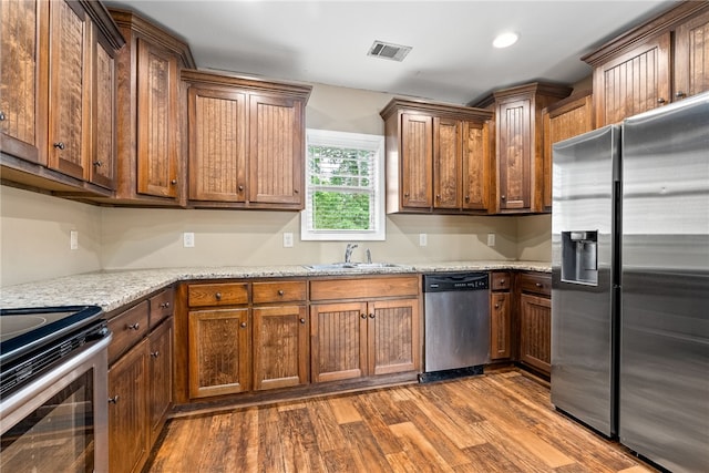 kitchen featuring appliances with stainless steel finishes, a sink, wood finished floors, light stone countertops, and recessed lighting