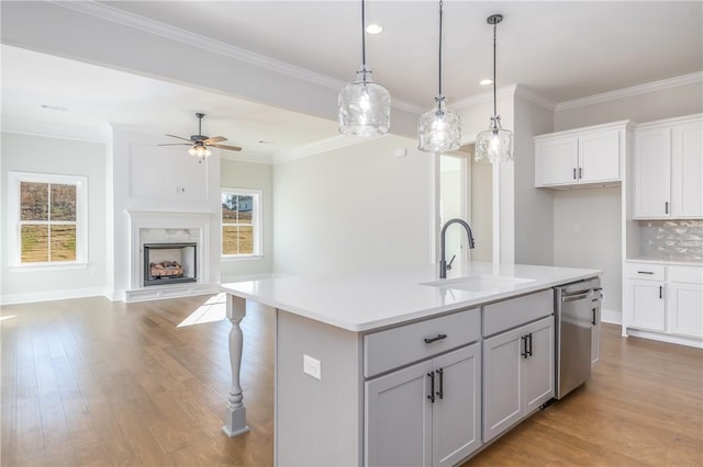 kitchen featuring tasteful backsplash, sink, dishwasher, hanging light fixtures, and an island with sink