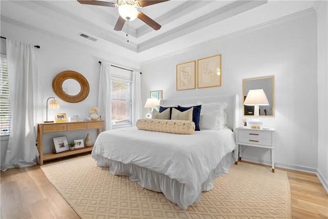 bedroom featuring ornamental molding, light wood finished floors, a tray ceiling, and visible vents