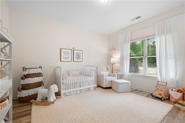 bedroom featuring a crib, baseboards, visible vents, and wood finished floors