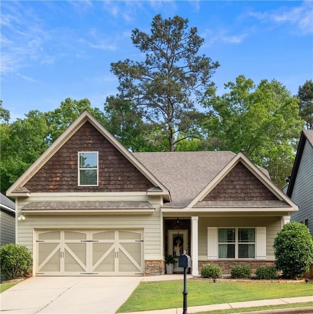 craftsman-style home featuring concrete driveway, a front yard, roof with shingles, and a garage