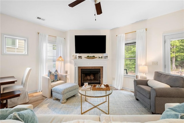 living room with a healthy amount of sunlight, a ceiling fan, visible vents, and a tile fireplace