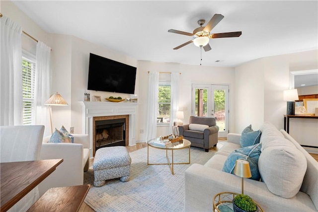 living area featuring a tile fireplace, light wood-type flooring, a ceiling fan, and a healthy amount of sunlight