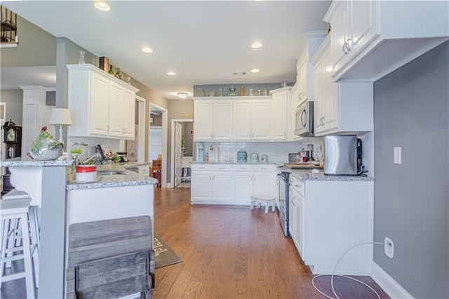 kitchen with light stone countertops, white cabinetry, kitchen peninsula, and appliances with stainless steel finishes