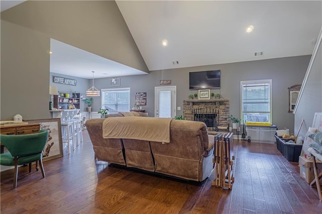 living room with a stone fireplace, dark hardwood / wood-style flooring, and high vaulted ceiling