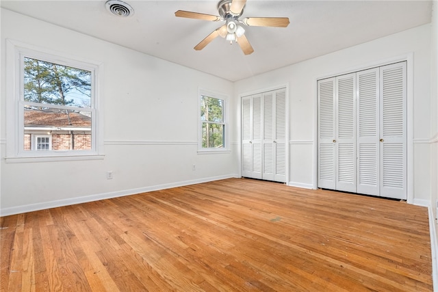 unfurnished bedroom featuring two closets, light hardwood / wood-style floors, and ceiling fan