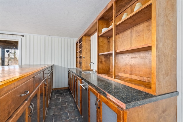 bar with sink, stainless steel dishwasher, and a textured ceiling