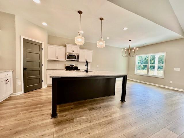 kitchen with pendant lighting, a kitchen island with sink, white cabinets, sink, and stainless steel appliances