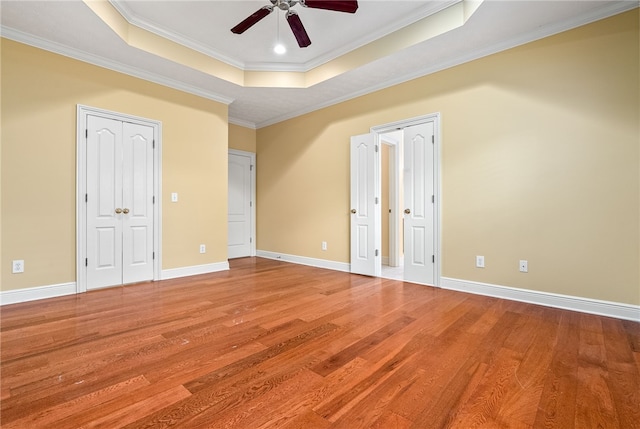 unfurnished bedroom with a raised ceiling, wood finished floors, baseboards, and ornamental molding
