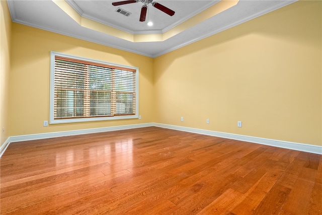 unfurnished room featuring a tray ceiling, wood finished floors, visible vents, ornamental molding, and ceiling fan