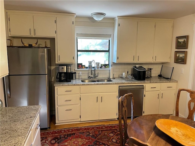 kitchen with backsplash, light stone countertops, sink, and stainless steel appliances