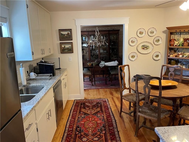 kitchen featuring decorative backsplash, appliances with stainless steel finishes, light stone counters, light hardwood / wood-style flooring, and white cabinets