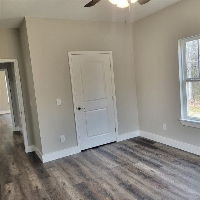 empty room with a healthy amount of sunlight, dark wood-type flooring, and ceiling fan