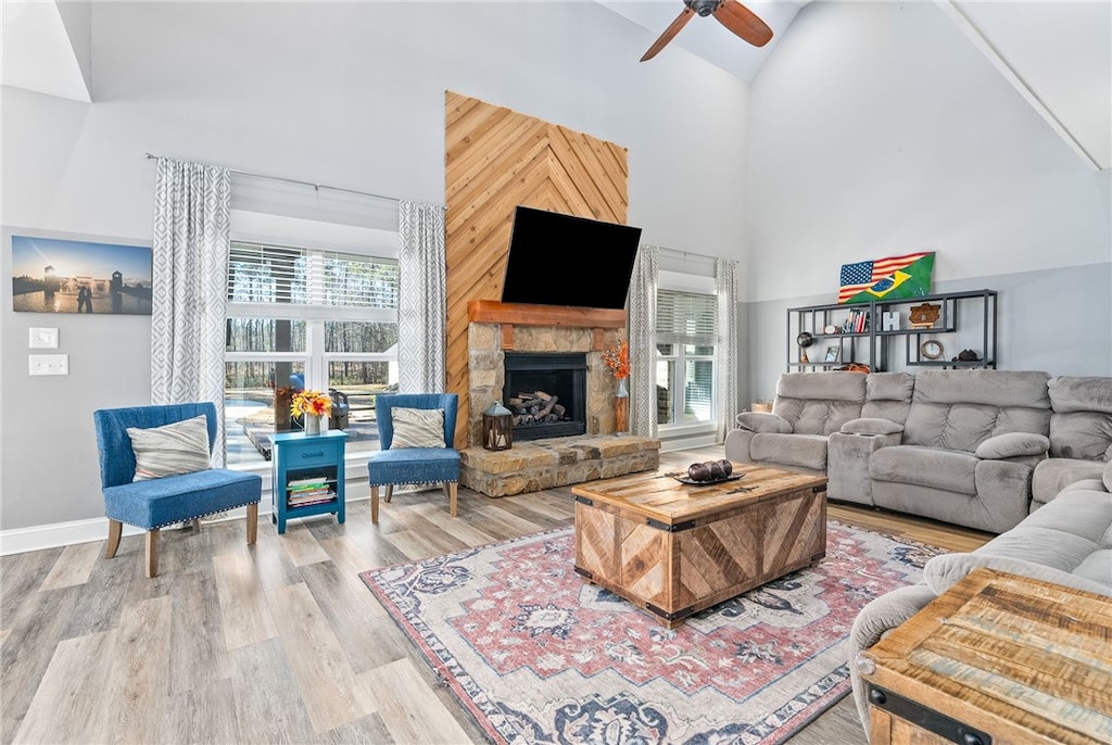 living area featuring high vaulted ceiling, a stone fireplace, wood finished floors, and a ceiling fan