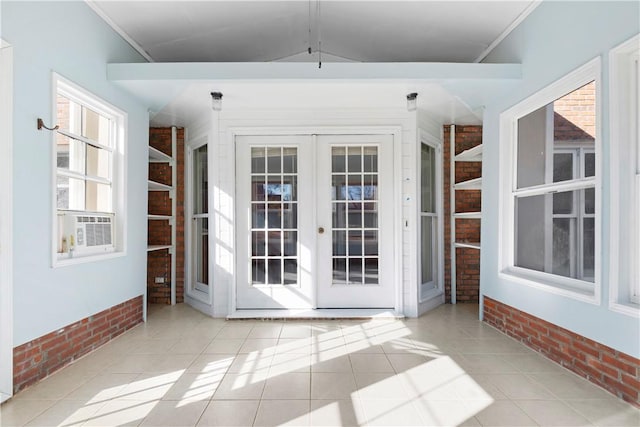 interior space with lofted ceiling, light tile patterned floors, a healthy amount of sunlight, brick wall, and french doors