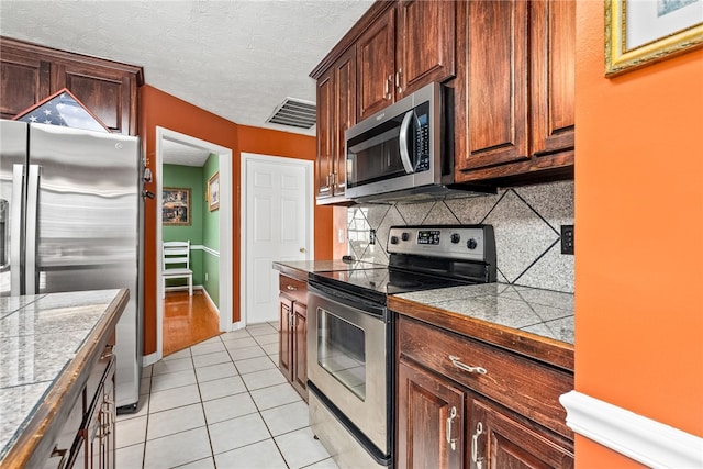 kitchen with backsplash, appliances with stainless steel finishes, light tile patterned flooring, and a textured ceiling