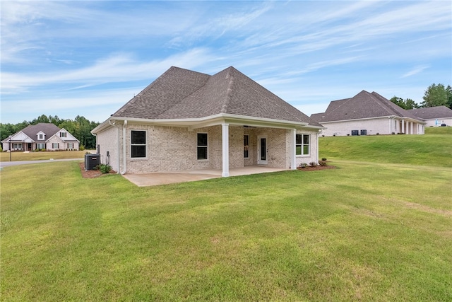 rear view of house with a lawn, roof with shingles, cooling unit, a patio area, and brick siding