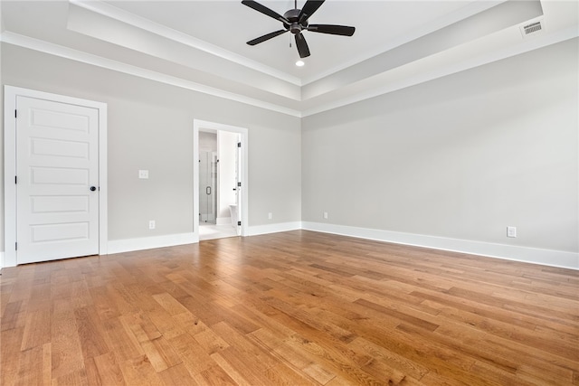 empty room featuring light wood-type flooring, a raised ceiling, visible vents, and baseboards