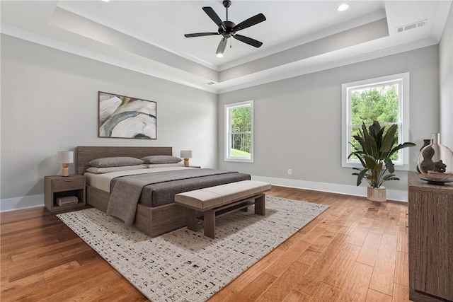 bedroom with a tray ceiling, light wood-type flooring, and visible vents