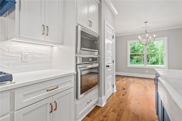 kitchen with light wood-style flooring, white cabinets, appliances with stainless steel finishes, decorative backsplash, and crown molding