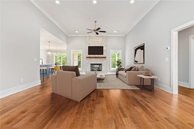 living area featuring ornamental molding, light wood-type flooring, a stone fireplace, and baseboards