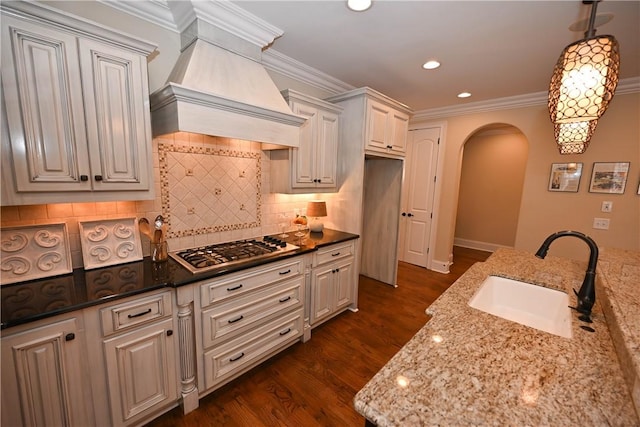 kitchen with dark stone counters, premium range hood, a sink, and arched walkways