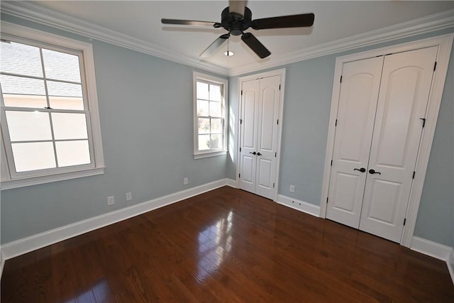 unfurnished bedroom with multiple closets, dark wood finished floors, baseboards, and ornamental molding