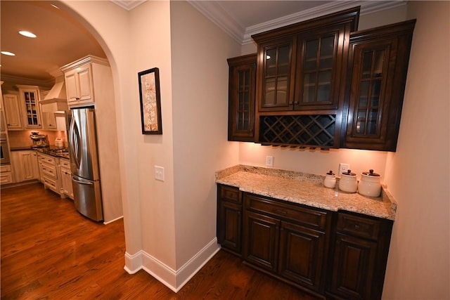 bar with dark hardwood / wood-style floors, stainless steel refrigerator, ornamental molding, and light stone counters