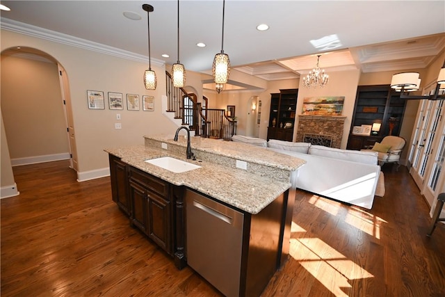 kitchen featuring arched walkways, an island with sink, light stone countertops, dark brown cabinets, and a sink