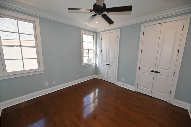 unfurnished bedroom with ornamental molding, wood finished floors, baseboards, and two closets