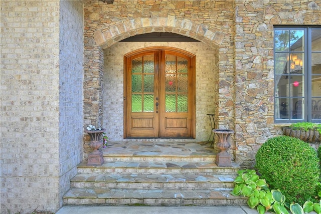 entrance to property featuring stone siding, french doors, and brick siding