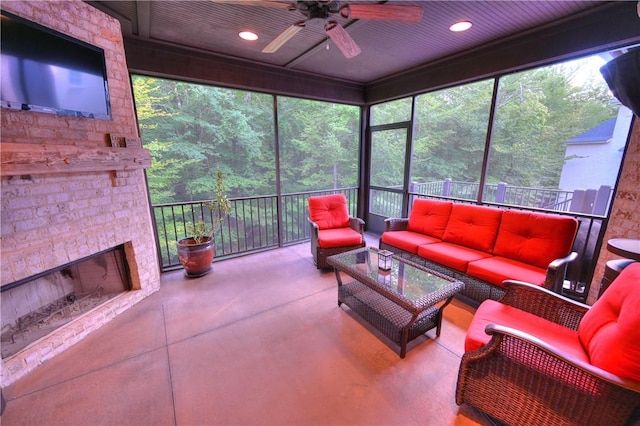 sunroom with an outdoor living space with a fireplace, ceiling fan, and a wooded view