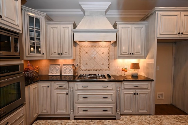 kitchen featuring tasteful backsplash, glass insert cabinets, custom range hood, crown molding, and appliances with stainless steel finishes