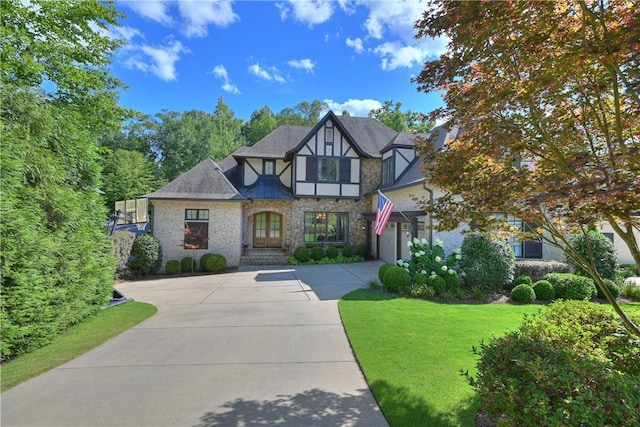 english style home featuring stucco siding, driveway, stone siding, a front yard, and a garage