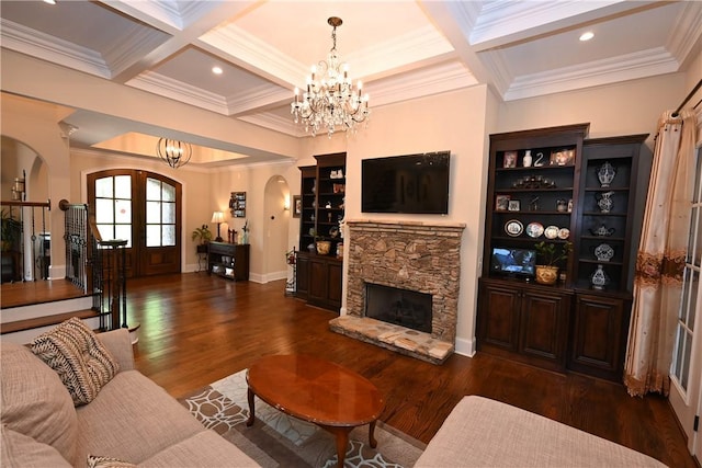 living room featuring an inviting chandelier, coffered ceiling, french doors, a stone fireplace, and beamed ceiling