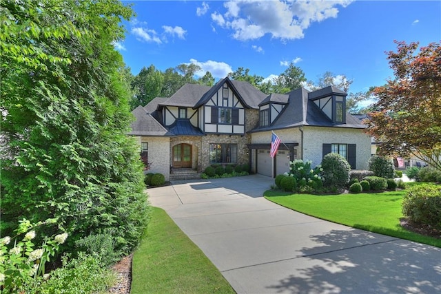 tudor house with an attached garage, concrete driveway, roof with shingles, stucco siding, and a front yard