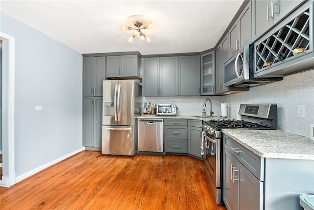 608 Edgewood Dr, Auburn, AL 36830 - kitchen featuring appliances with stainless steel finishes, gray cabinets, light wood-style floors, glass insert cabinets, and light stone countertops