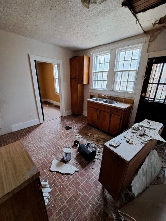 kitchen with brick floor, brown cabinets, a sink, a textured ceiling, and baseboards