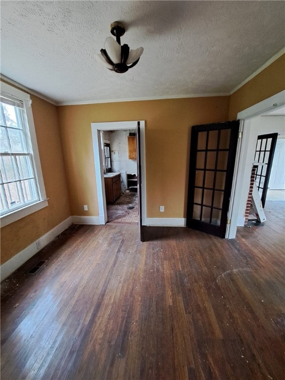 unfurnished room featuring wood-type flooring, visible vents, ornamental molding, a textured ceiling, and baseboards